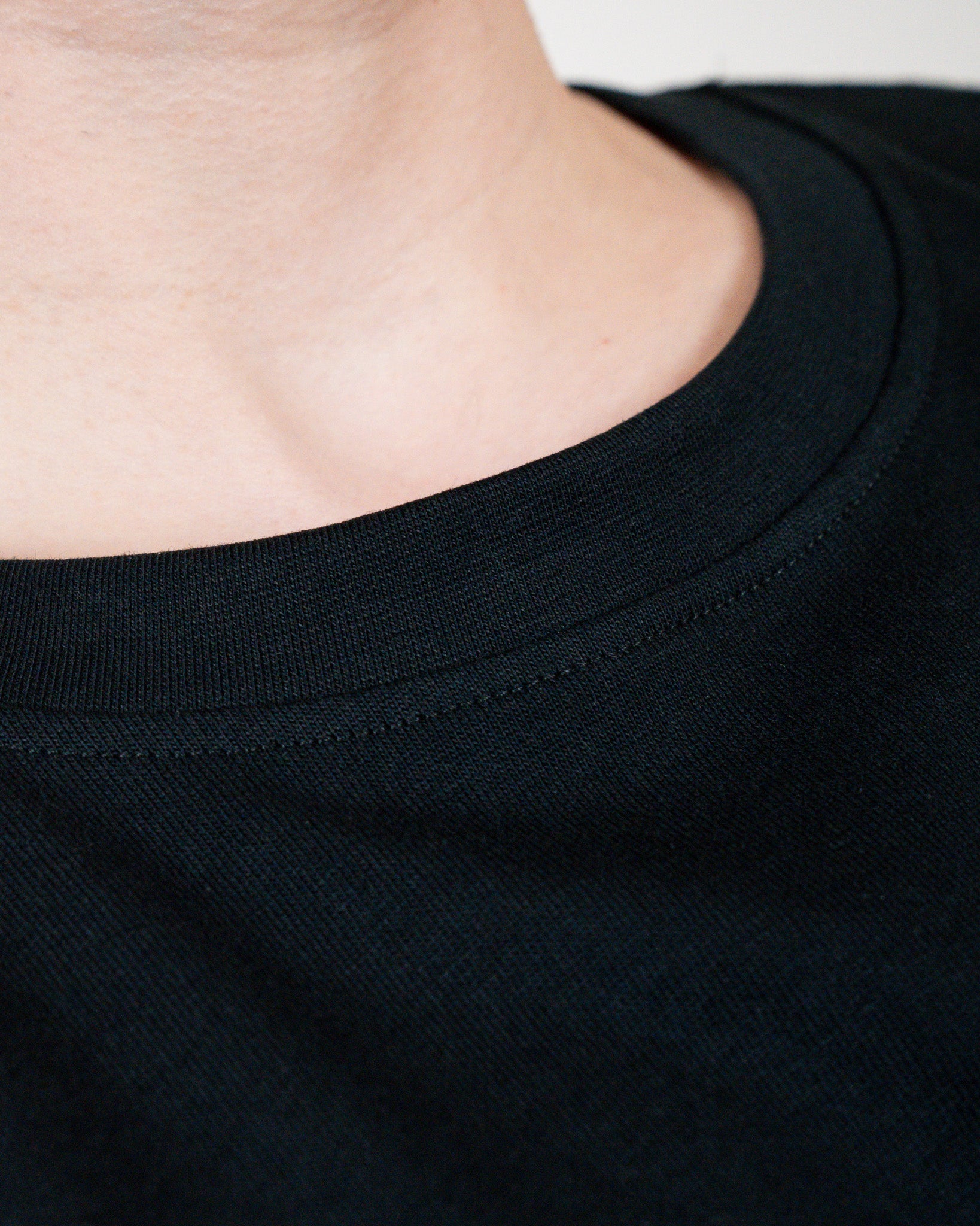 Nahaufnahme des runden Halsausschnitts des schwarzen T-Shirts, der sauber vernäht ist. Der Stoff zeigt eine feine, dichte Struktur und liegt eng am Hals.