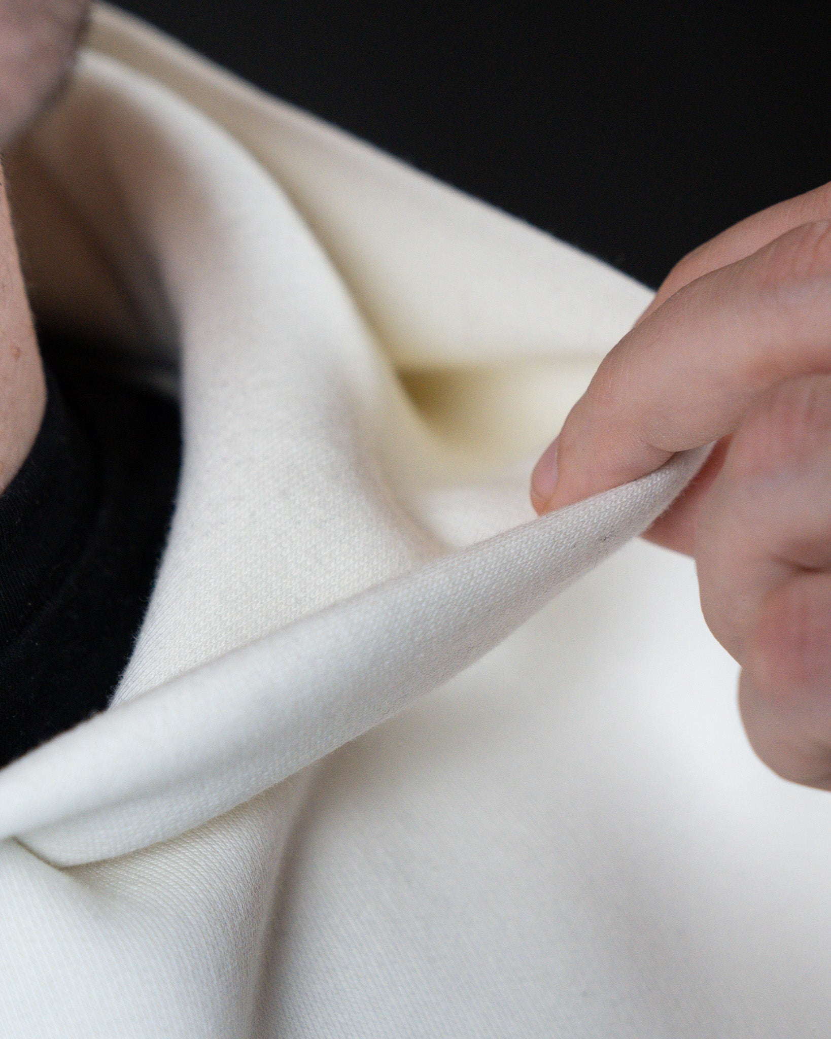Close-up der Kapuzenkante des weißen Hoodies, bei dem die Doppellagigkeit des Materials sichtbar wird.