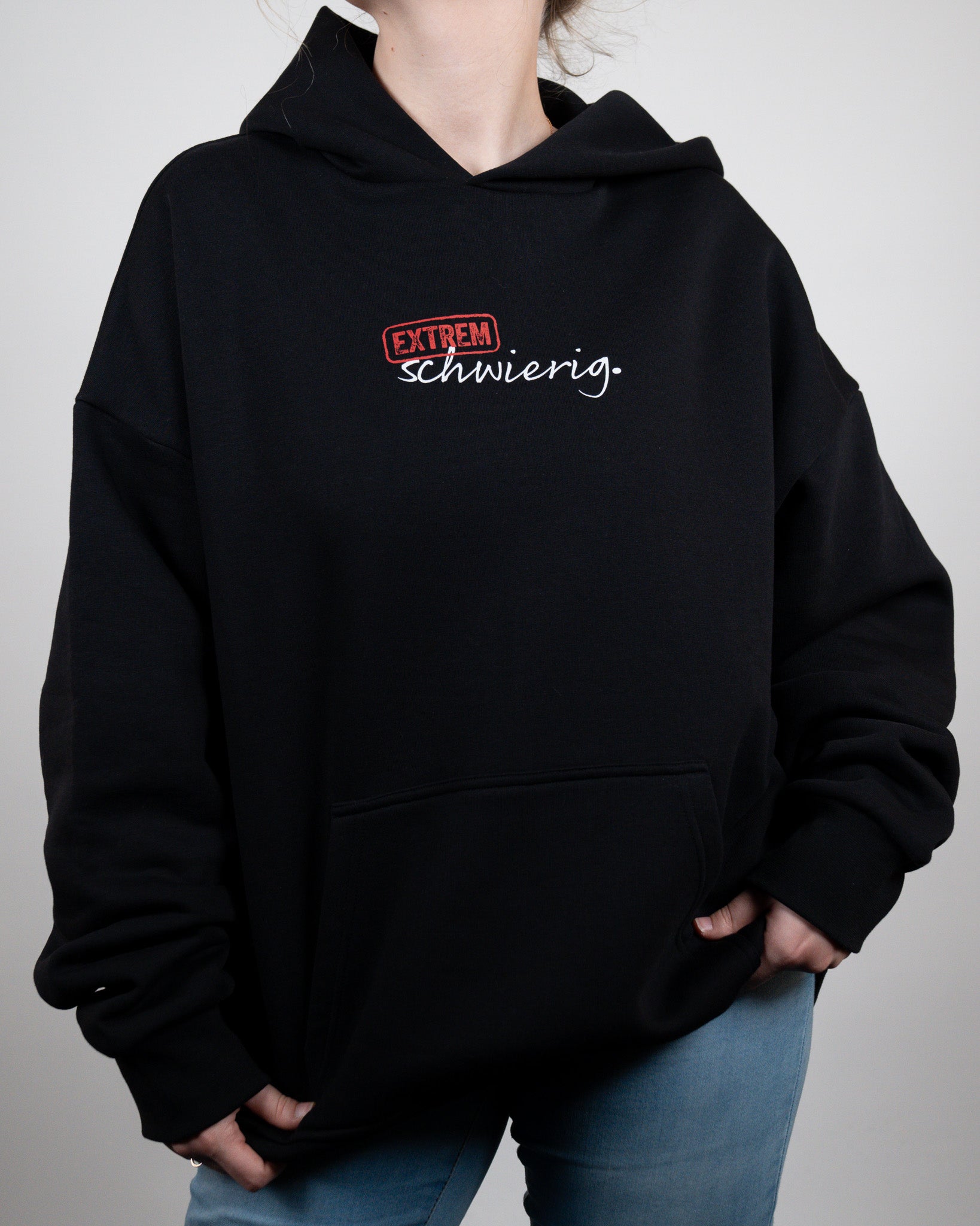 Schwarzer Hoodie mit „EXTREM schwierig.“-Print in rot und weiß, locker getragen mit lässigem Look. Fokus auf das Frontdesign.