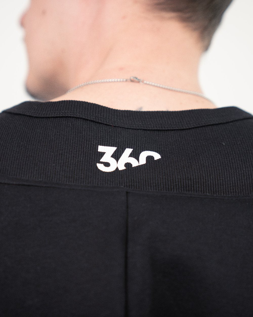 Detailansicht des oberen Rückenteils eines schwarzen Tanktops. Nahe unterhalb des Kragens ist ein weißer „360“-Schriftzug mittig aufgedruckt.