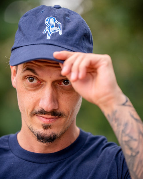 Navyblaue Baseballcap mit weißer Stickerei eines klassischen Monobloc-Stuhls auf der Vorderseite, frontal getragen, leicht nach unten gezogen.
