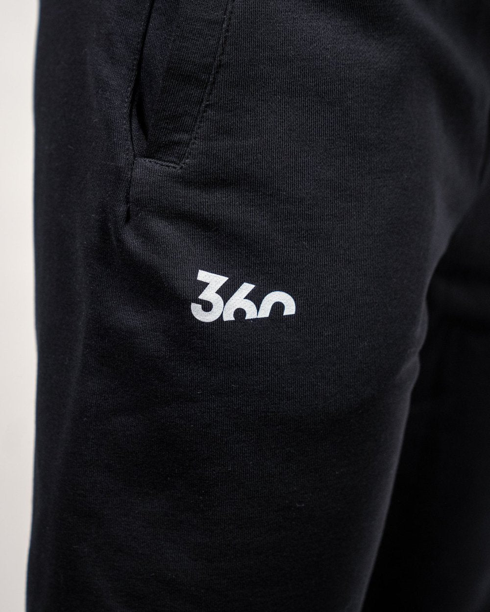 Nahaufnahme des weißen „360“-Logos auf dem linken Oberschenkel der schwarzen Jogginghose aus weicher Baumwolle.