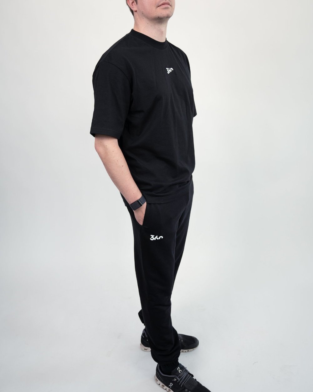 Komplettes Outfit bestehend aus schwarzem T-Shirt und schwarzer Jogginghose mit „360“-Logo, getragen von einer Person in sportlicher Pose mit Händen in den Taschen.