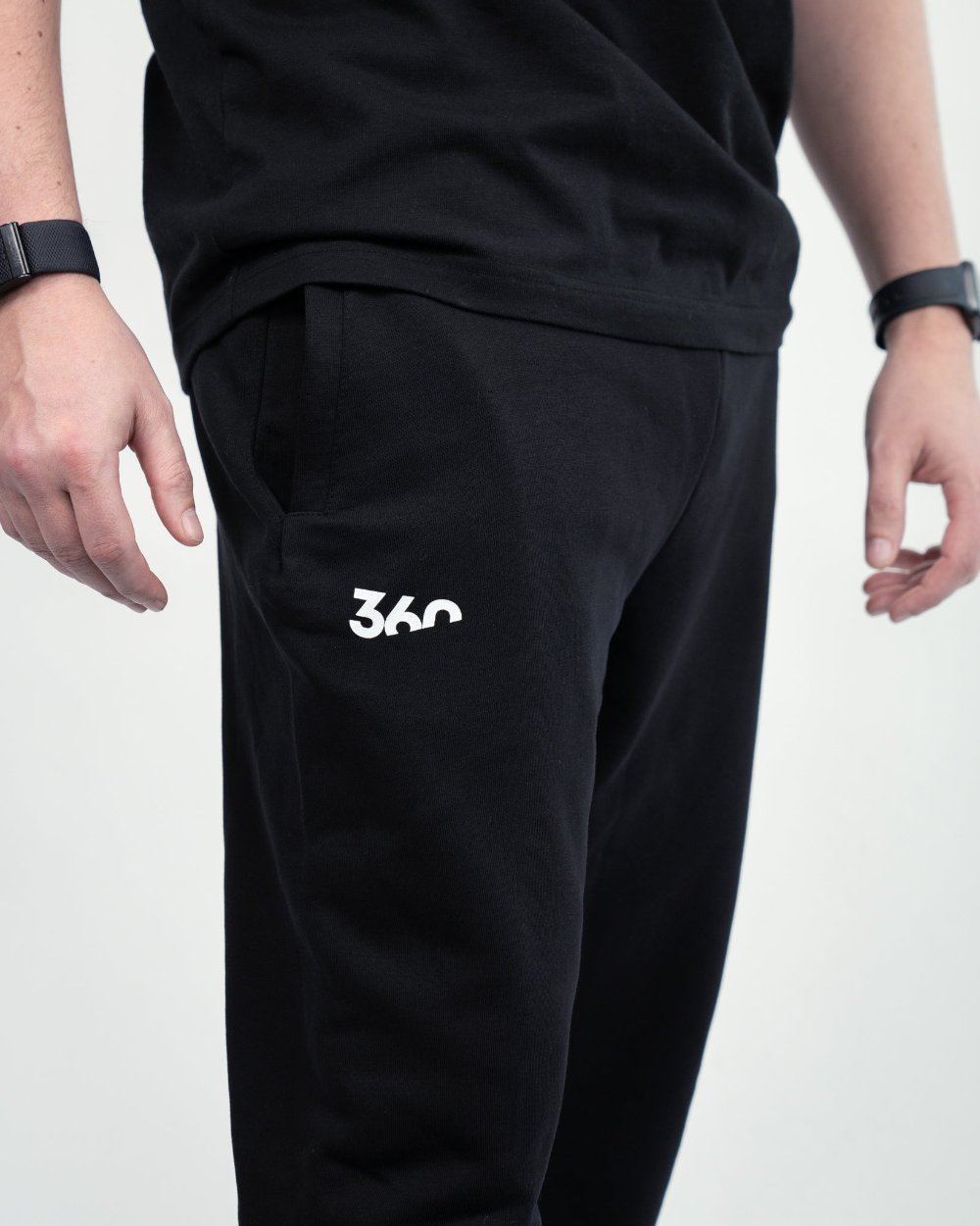Halbnahe Aufnahme der schwarzen Jogginghose mit sichtbarer Eingrifftasche und dem weißen „360“-Logo links oberhalb des Knies.