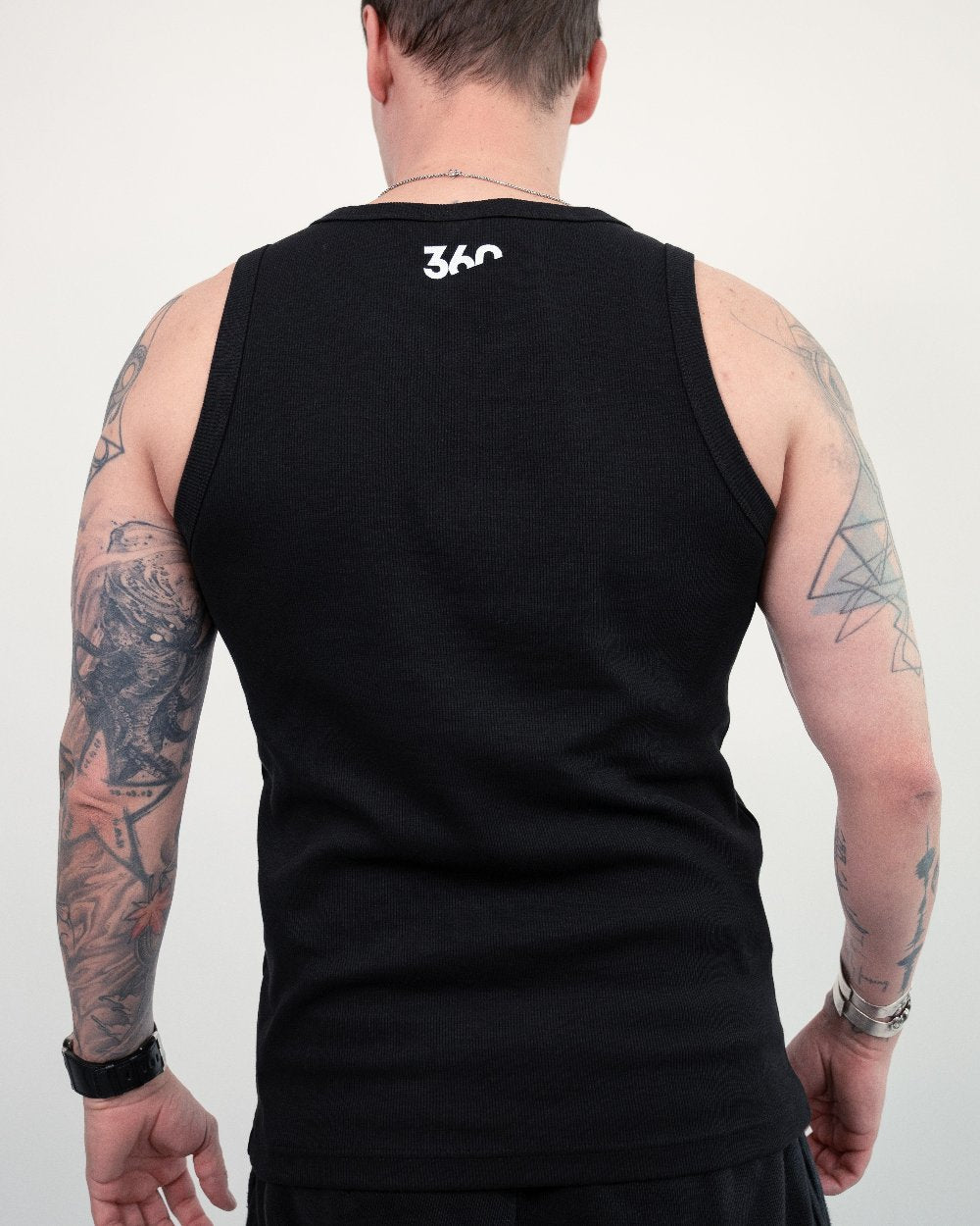 Rückenansicht eines schwarzen Tanktops mit weißem „360“-Print im Nackenbereich. Die tätowierten Arme und Schultern der Person sind sichtbar.