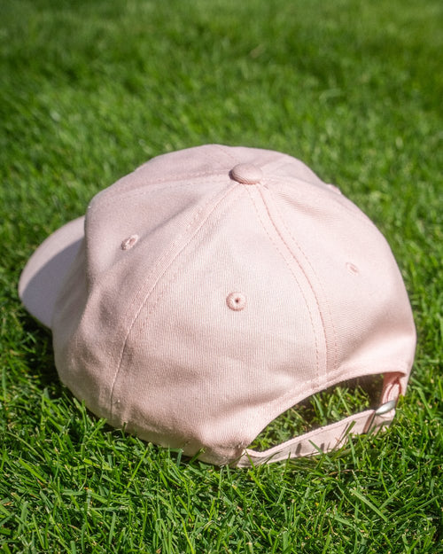 Rückansicht einer rosa Basecap auf grünem Rasen. Die Cap verfügt über einen verstellbaren Riemen und ist ohne Motiv auf der Rückseite.